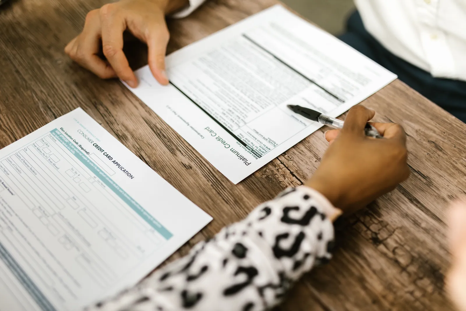 Close-up of two people reviewing and filling out a credit card application on a wooden table