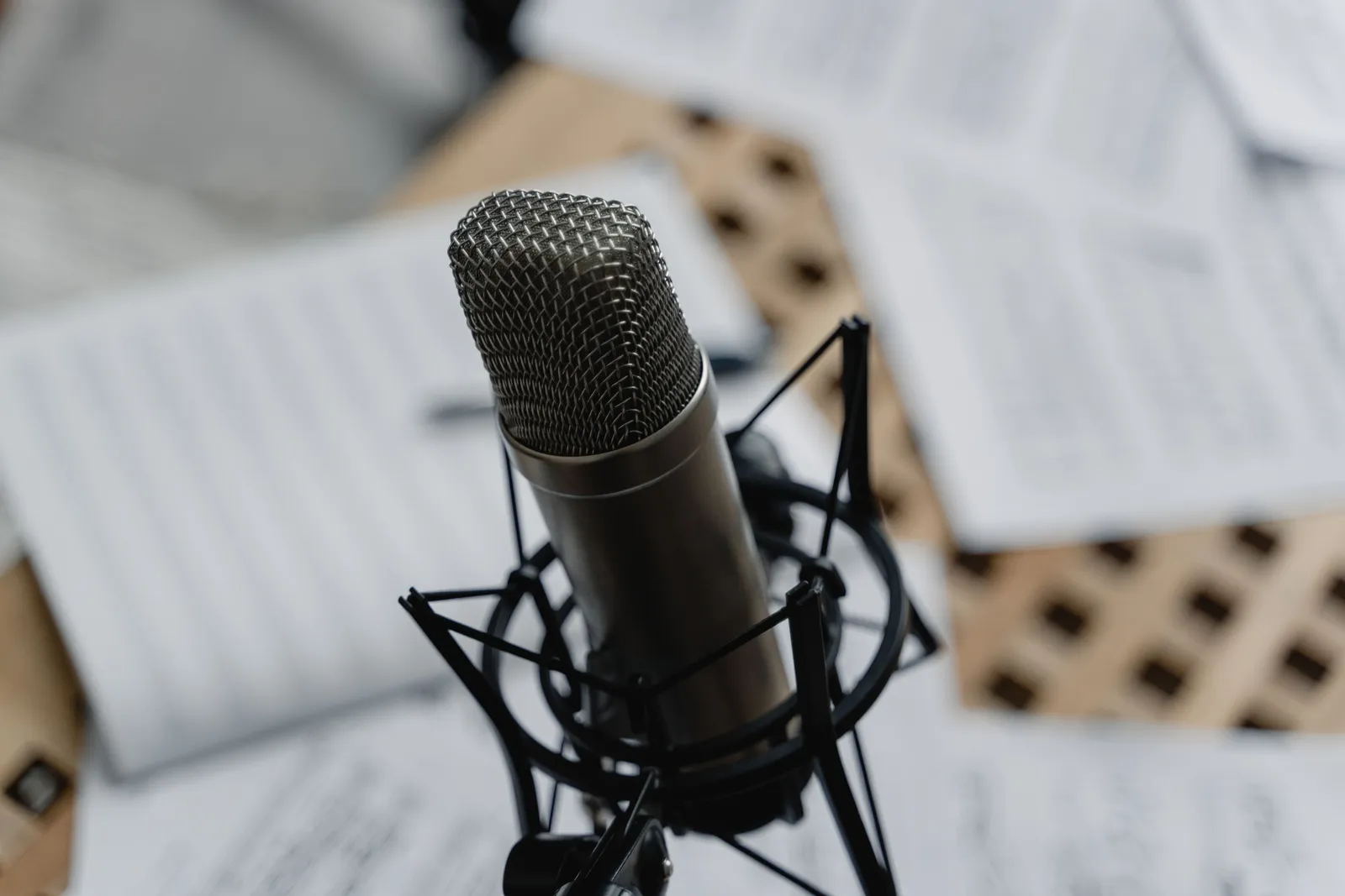 Close-up of a condenser microphone on a mic stand surrounded by music sheets in a studio setting