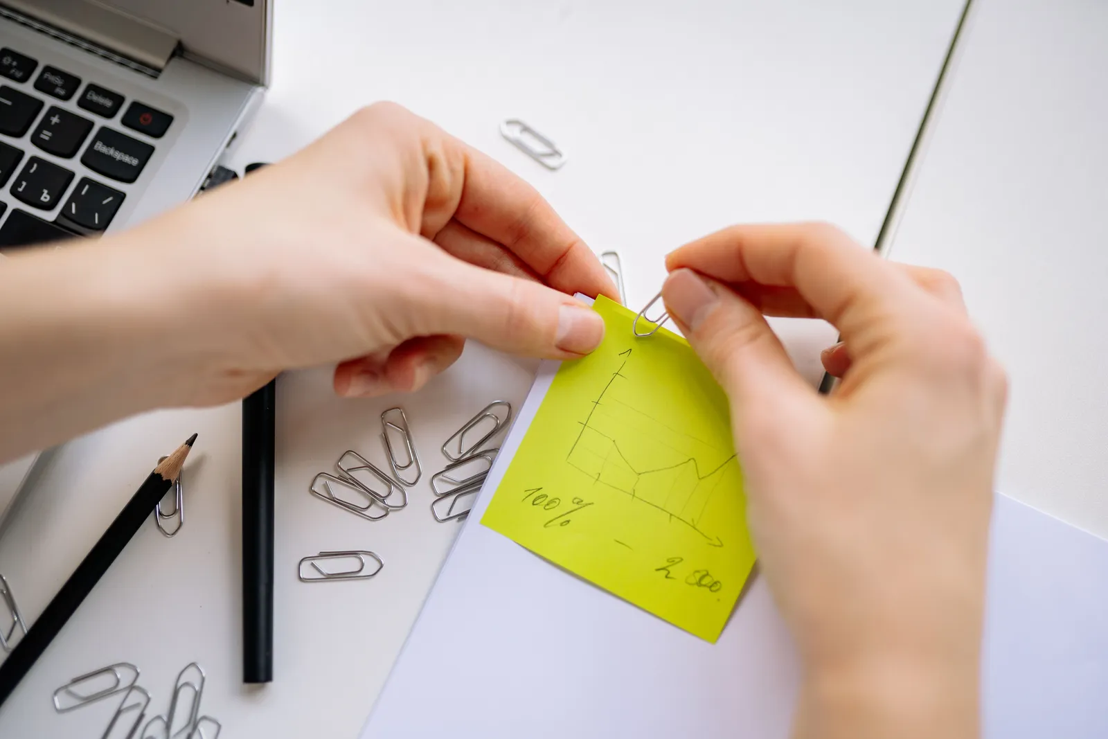 Close-up of hands attaching a paperclip to notes with a chart in a bright office environment
