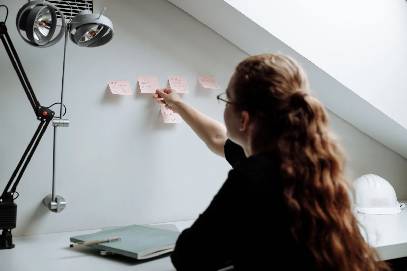 A woman organizes sticky notes on a wall in a sleek and modern office setting, promoting productivity and focus