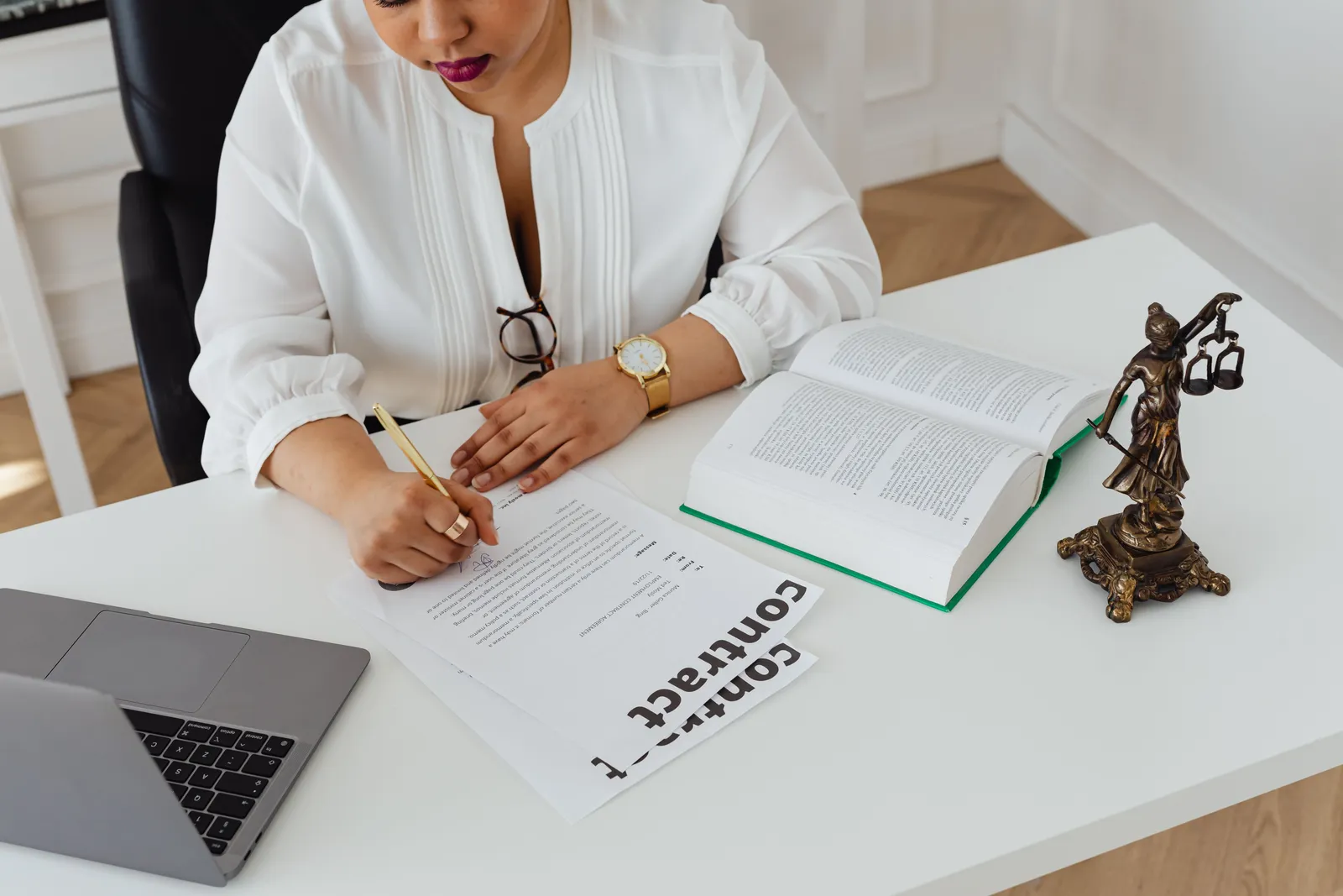 Woman in office writing on contracts, with law books and laptop on table