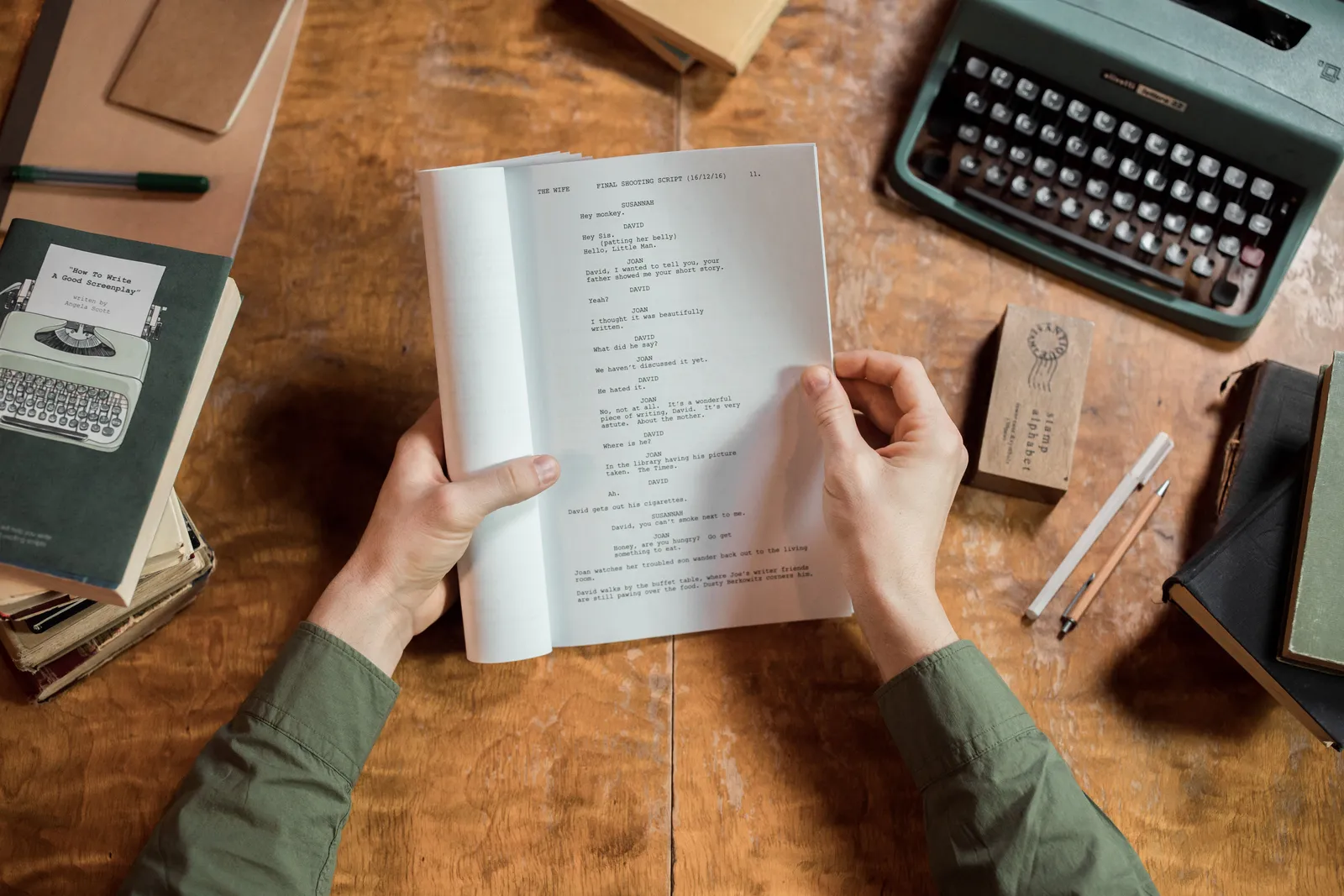 Hands holding script page at vintage desk with typewriter and books