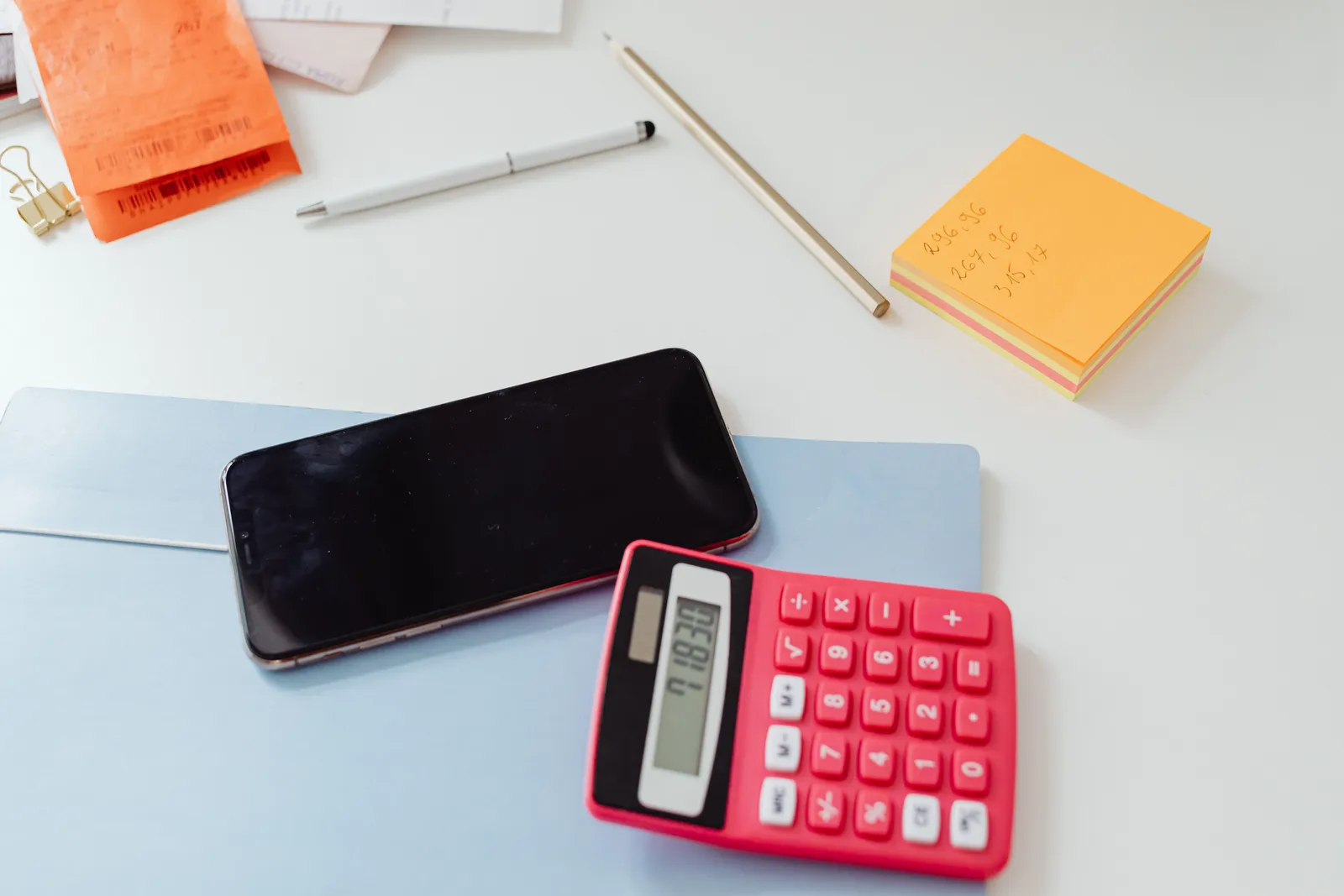 An organized office desk featuring a calculator, smartphone, and sticky notes on a white surface