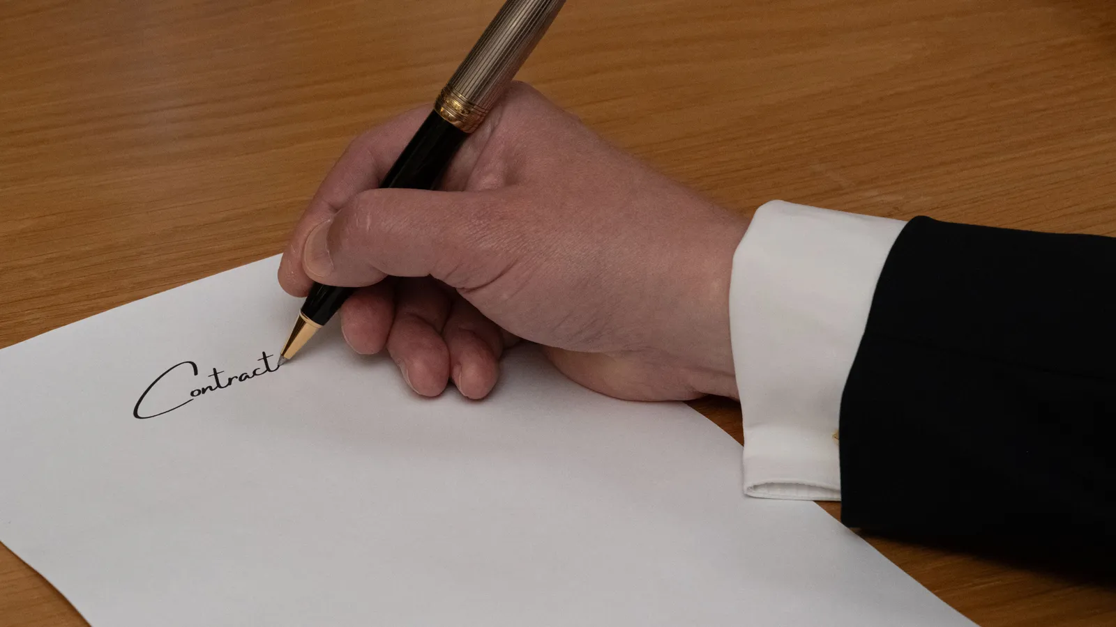 A professional signing a business contract with a fountain pen on a wooden desk