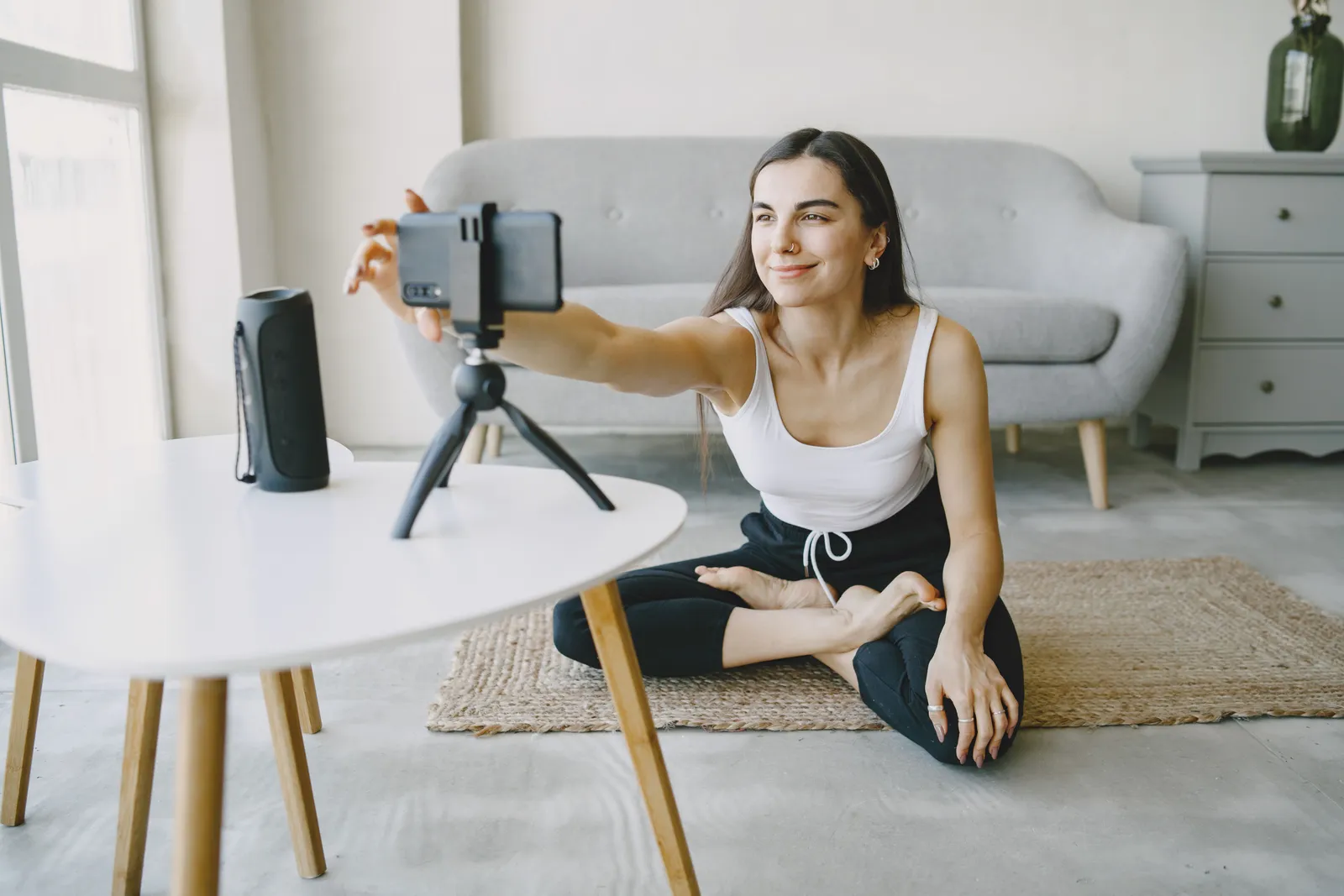 Smiling woman in a tank top vlogging indoors using a smartphone and tripod setup