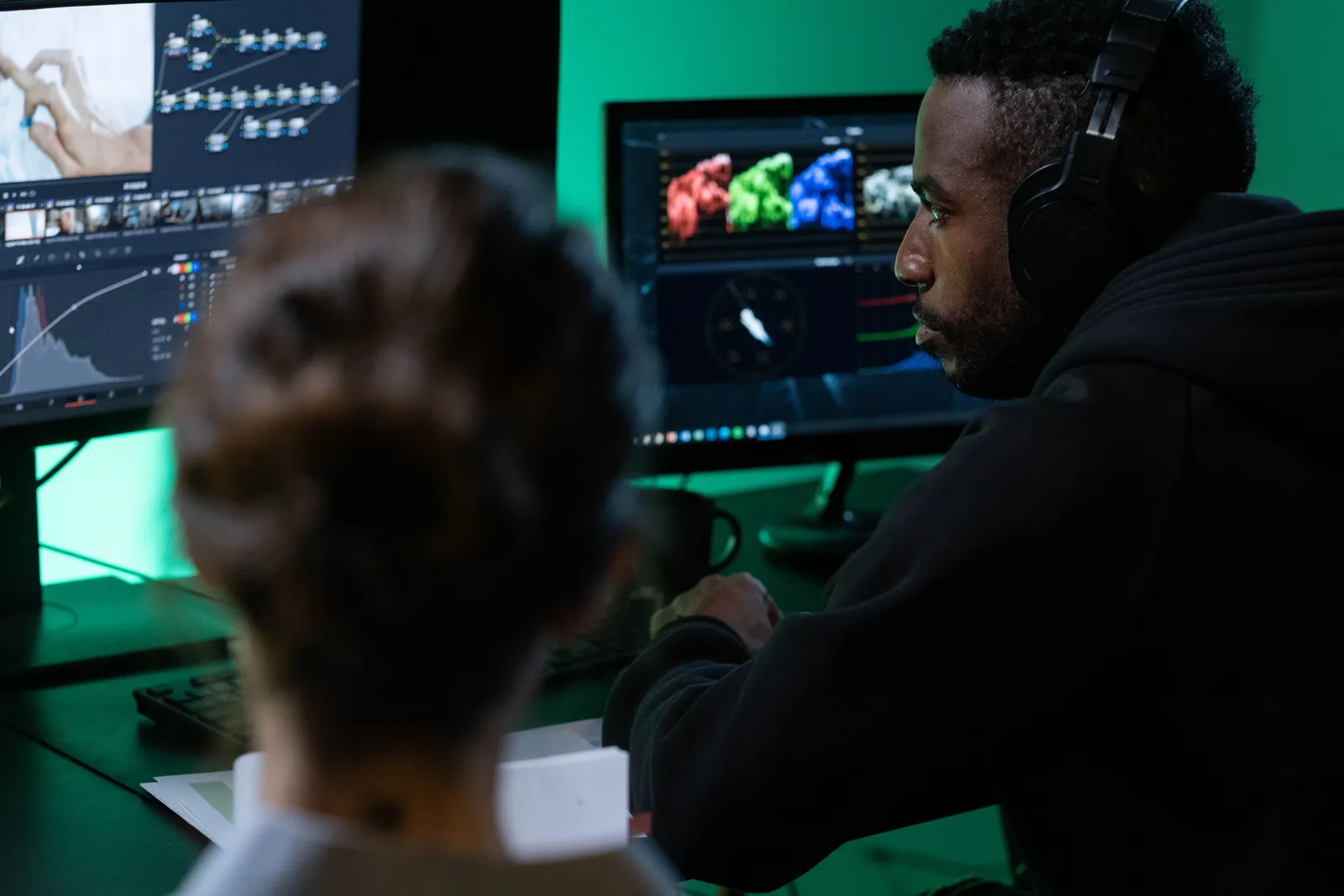 A man wearing headphones works on video editing with dual monitors in a dimly lit room