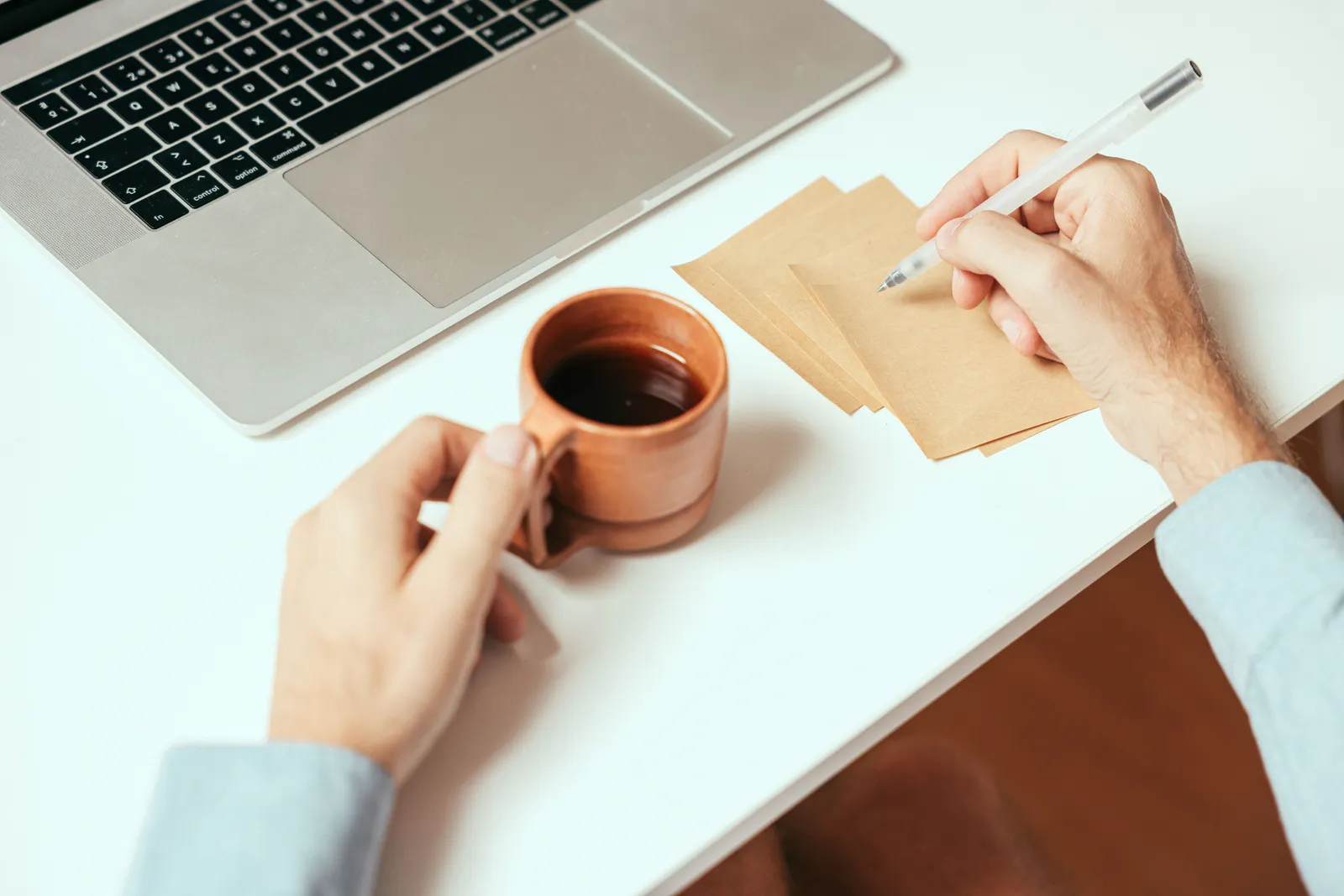 A person taking notes with coffee and a laptop on a home workspace desk