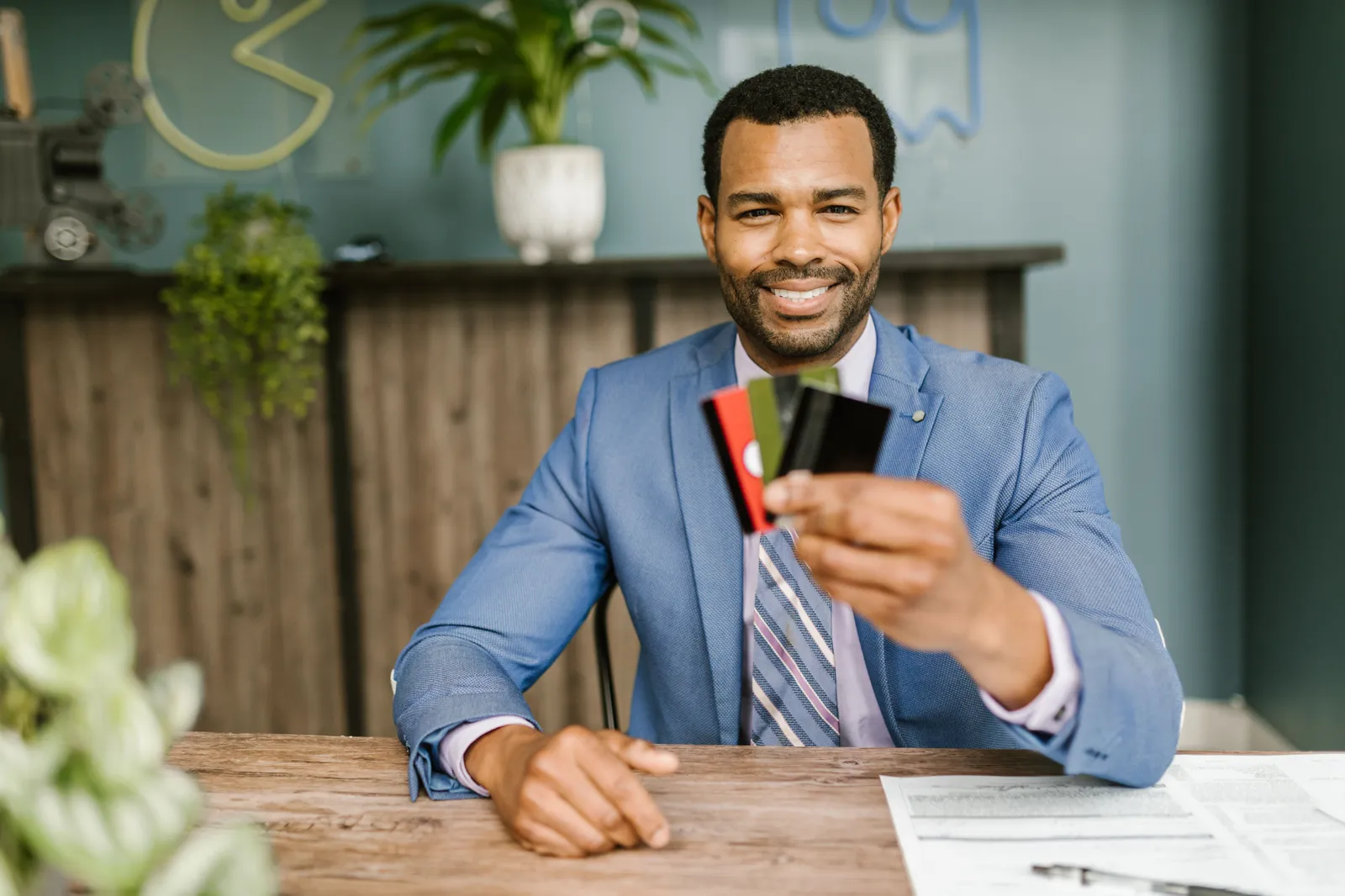 Smiling man in a suit holding credit cards at a business desk
