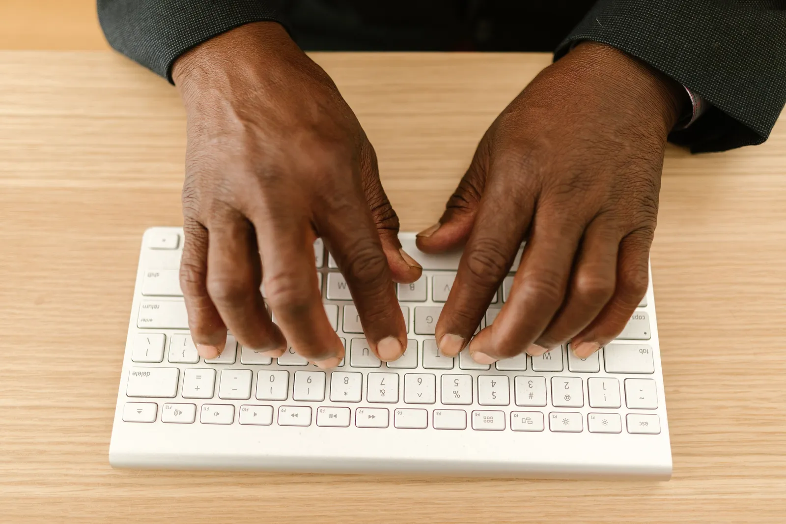 Close-up of hands typing on a wireless keyboard on a wooden desk