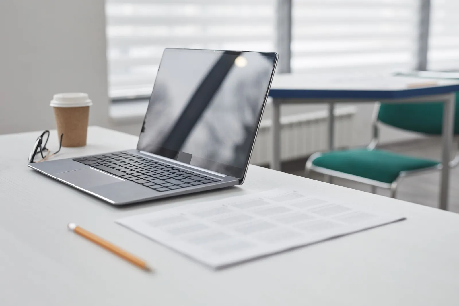 A sleek laptop on a clean white desk, accompanied by a coffee cup, pencil, and glasses in a modern office