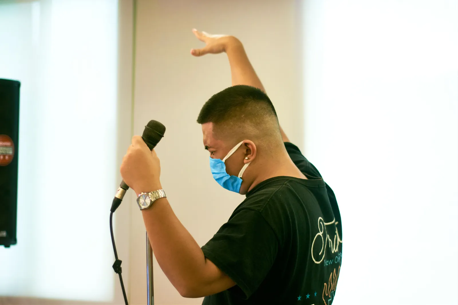 Male artist in black t-shirt and face mask singing into a microphone passionately