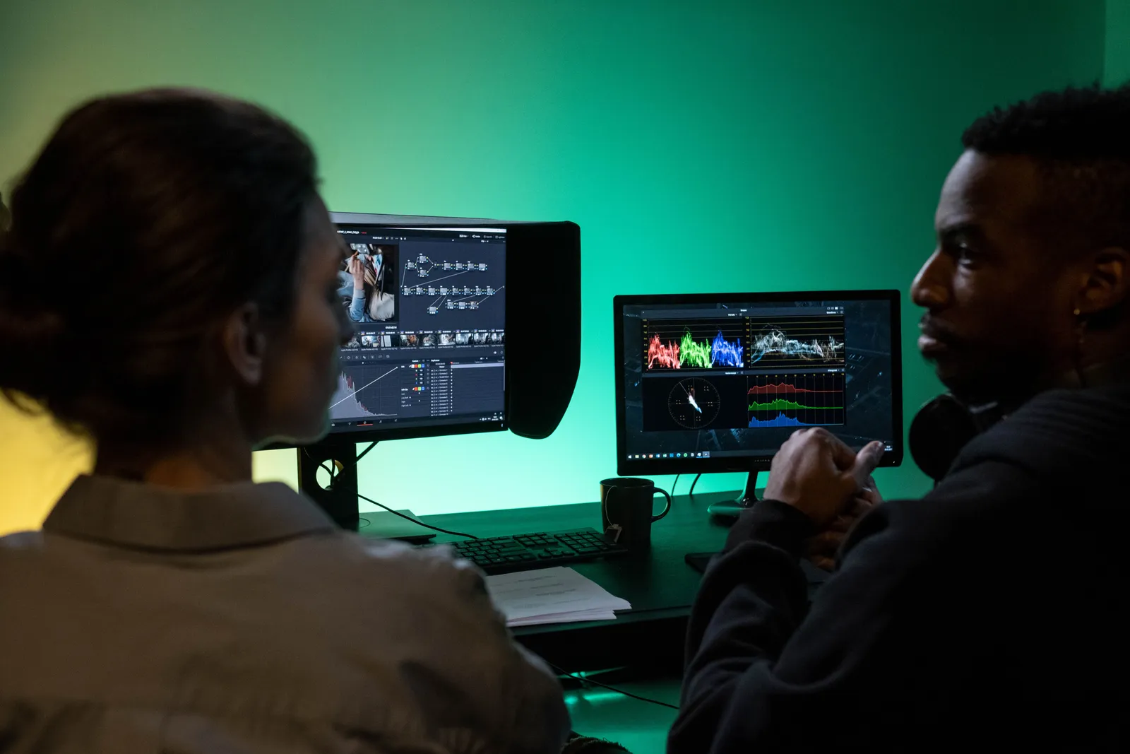 Two colleagues collaborating on video editing, analyzing color grading on dual monitors in a studio