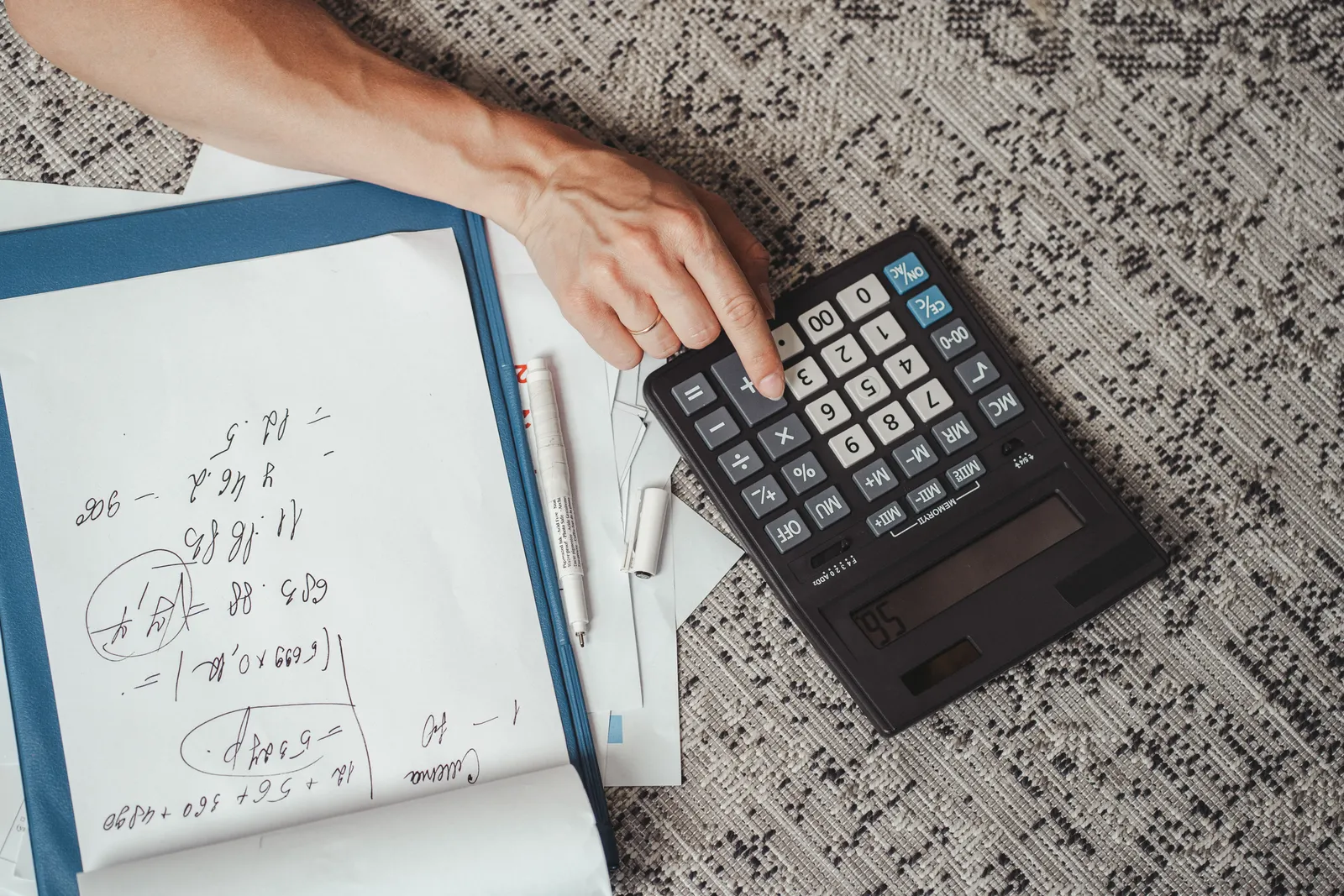 Top view of a hand calculating numbers with a large calculator and notes on a desk