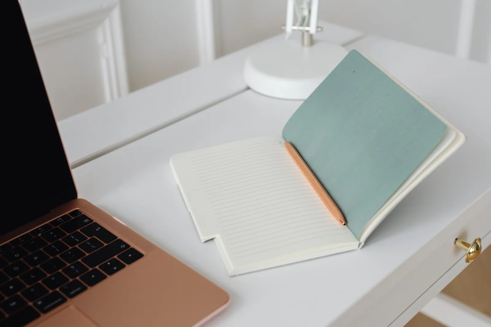Minimalist workspace with an open notebook, pen, and laptop on a white desk