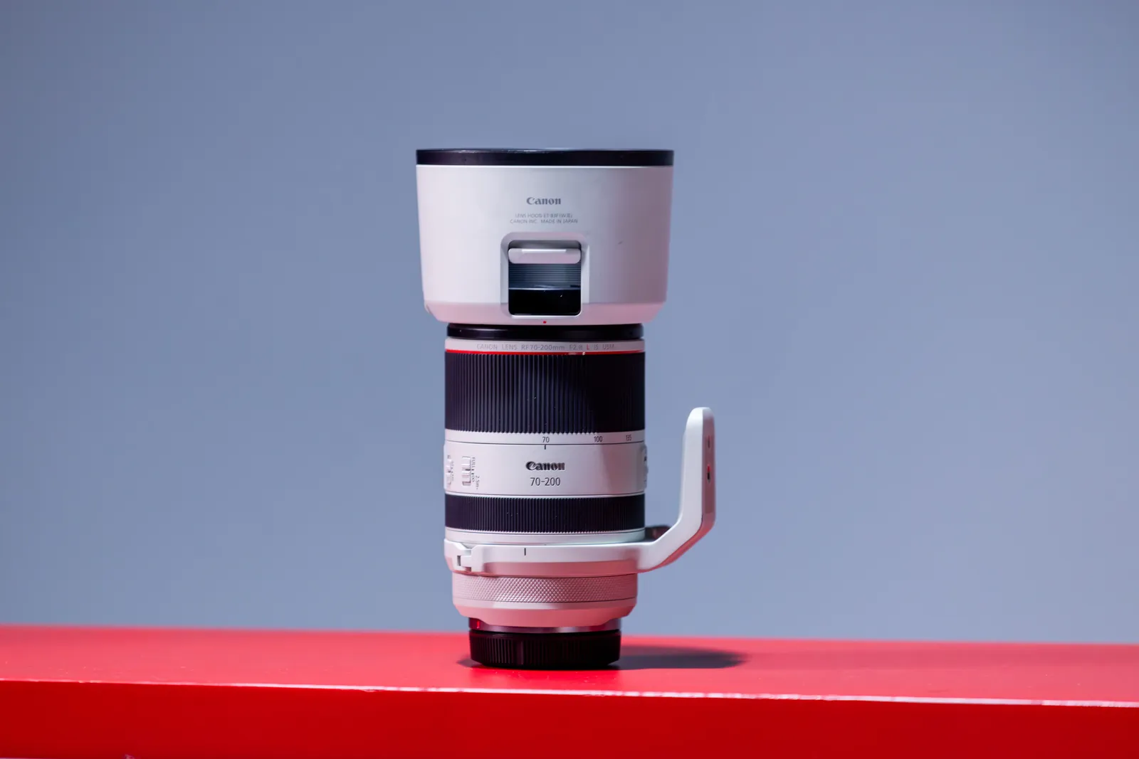 Close-up of a single camera lens standing on a red surface against a plain background