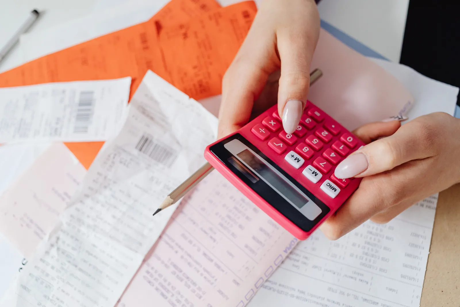 Hands using a pink calculator to manage expenses amidst various receipts and documents