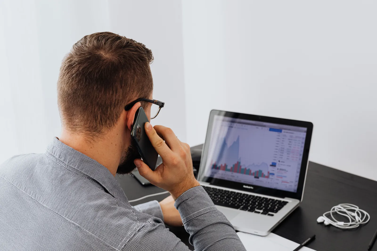 Businessman analyzing stock market data on a laptop while talking on the phone at his desk
