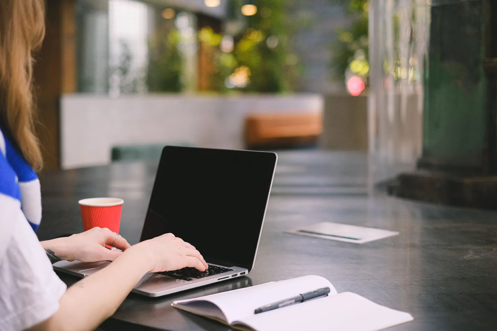 Person typing on a laptop in a modern indoor workspace with coffee and notebook