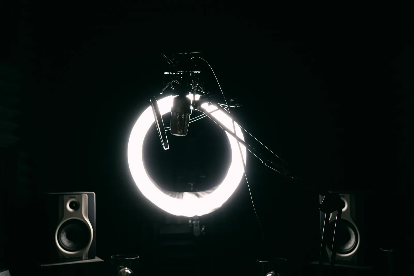 Dark studio room with condenser microphone, ring light, and speakers for recording purposes