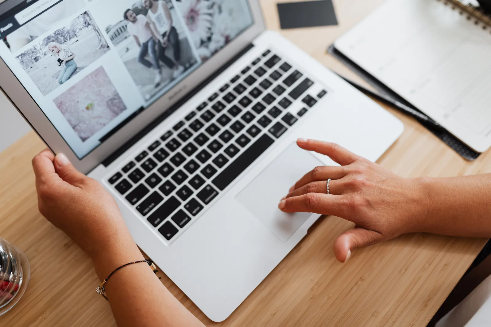 Close-up of hands browsing photos on a laptop at a wooden desk, showcasing internet browsing at work