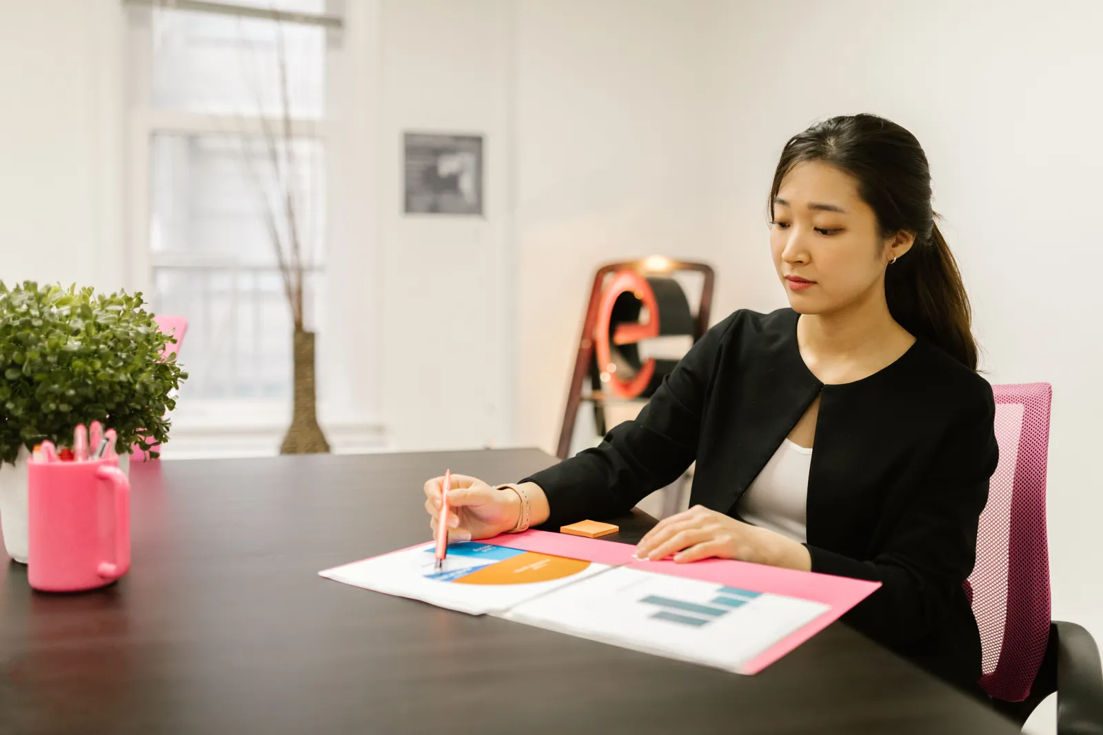 Woman in business attire analyzing documents at her office desk with reports and graphs