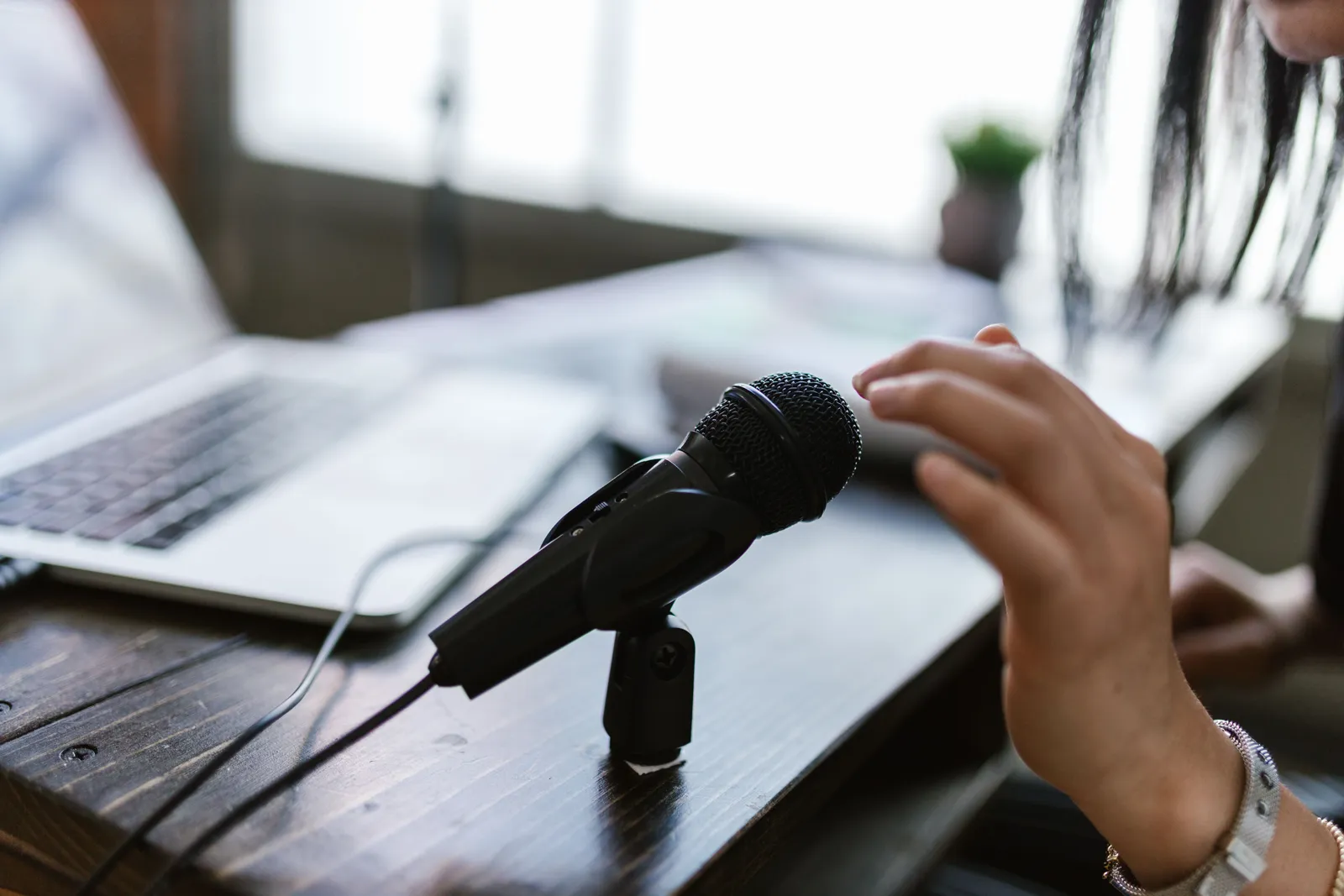 Close-up of a microphone and hand near a laptop, ideal for podcasting themes