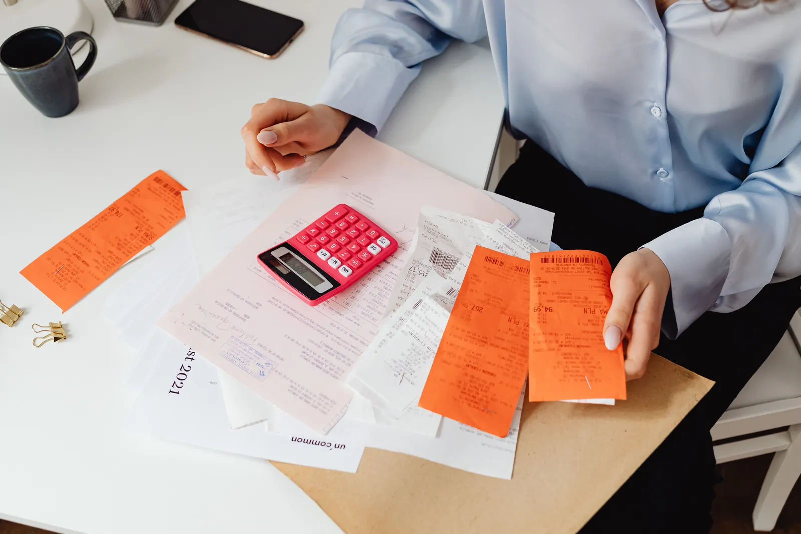 A woman reviews receipts and calculates expenses at a desk with a pink calculator