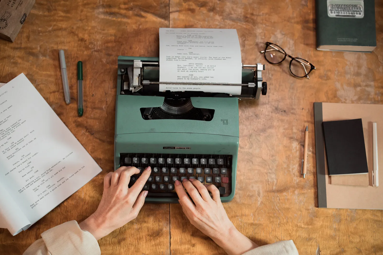 Hands typing on a classic typewriter with documents and stationery on a wooden table