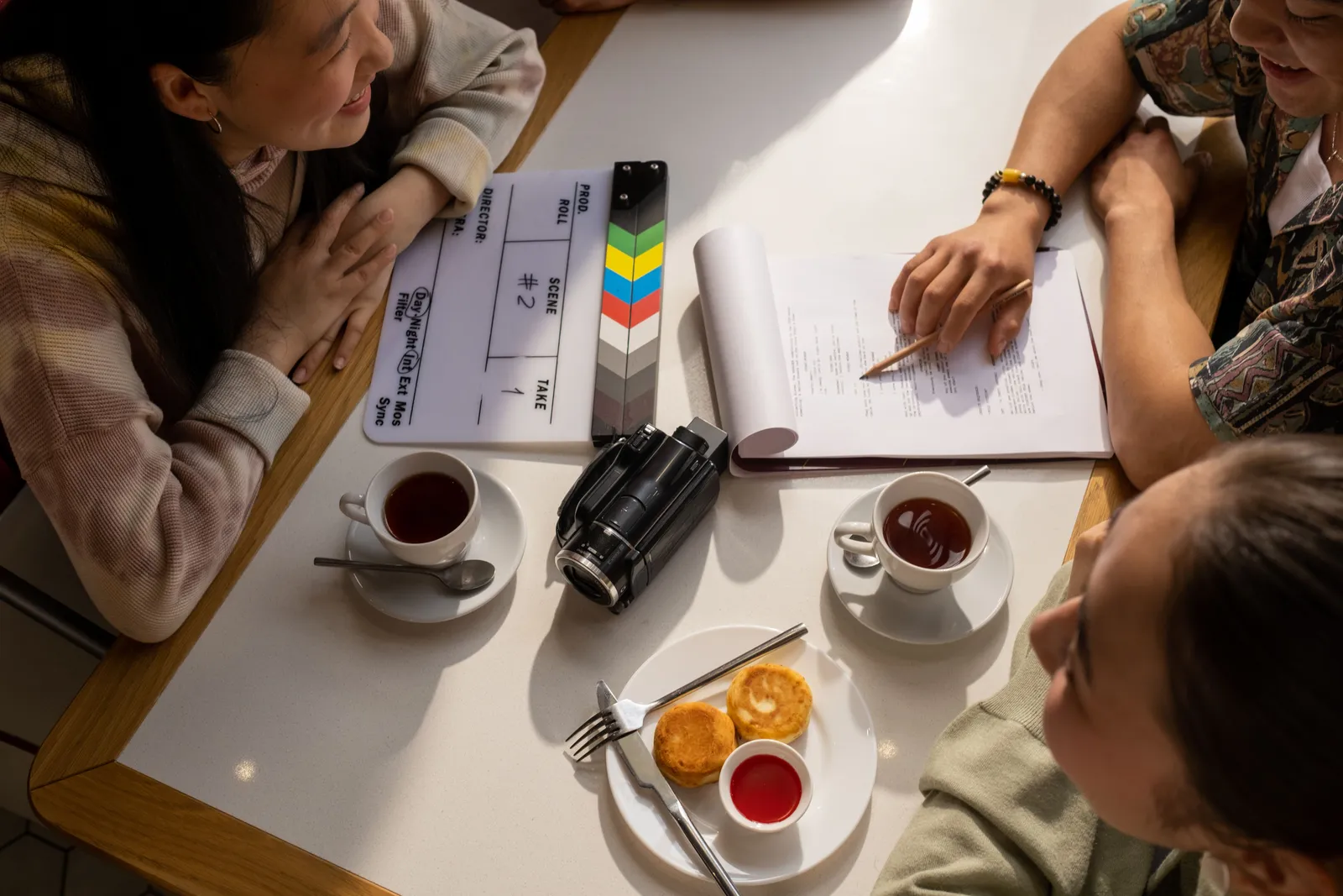 Team discussion over script with a clapperboard, camera, and coffee on a table