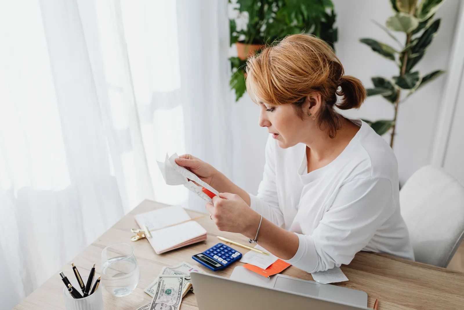 Woman sitting at a desk managing finances with a calculator and paper receipts in an office setting