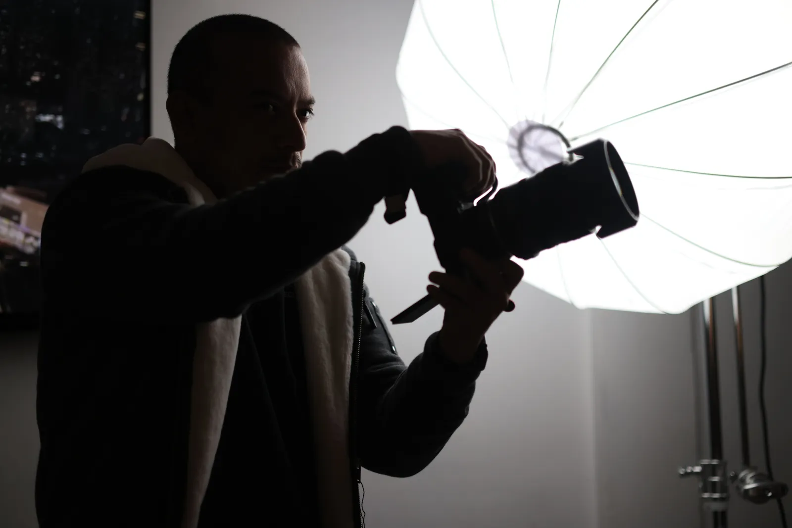 Silhouette of a photographer adjusting a camera during a studio shoot with a large umbrella light
