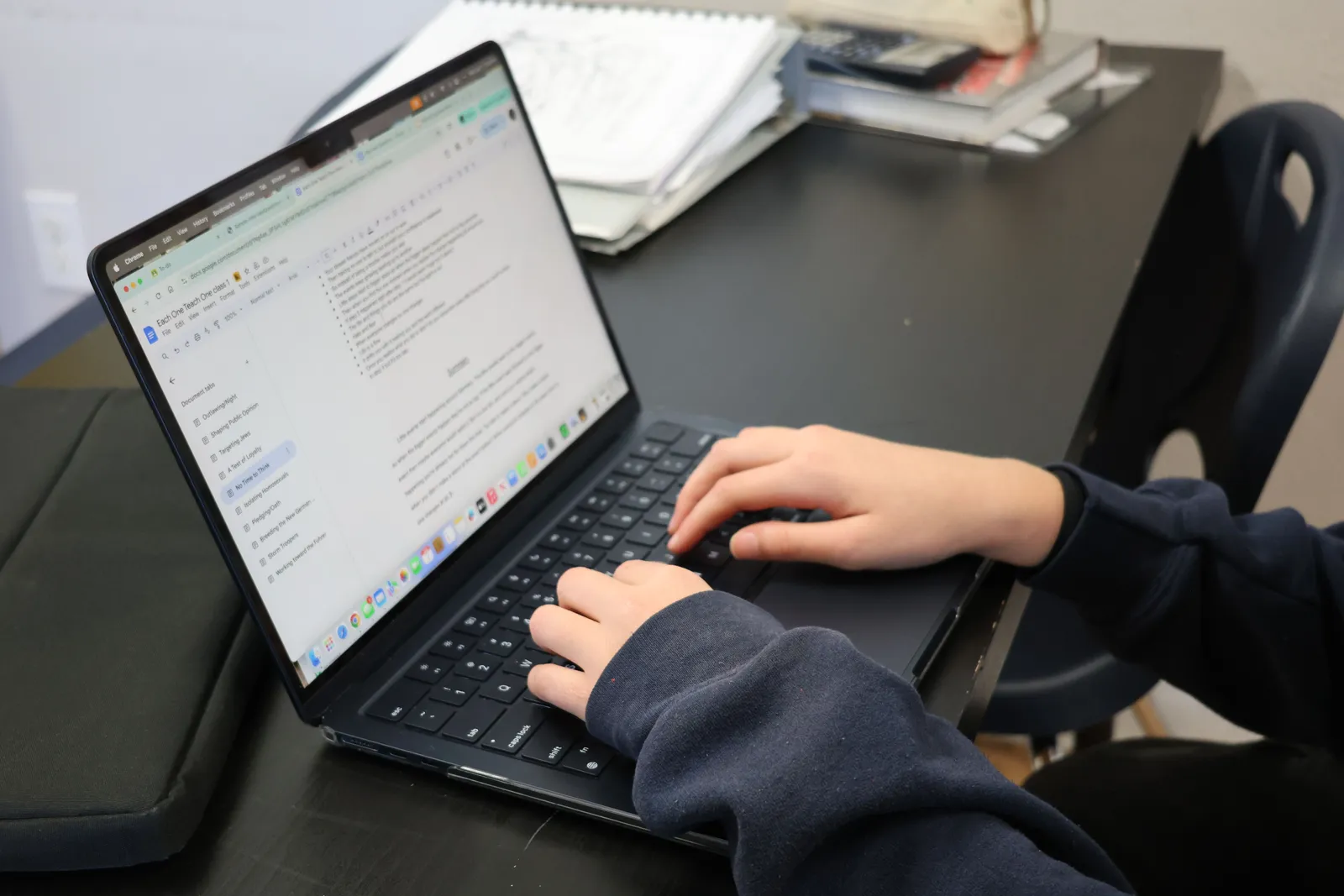 Person typing on a laptop at a desk with papers and books nearby