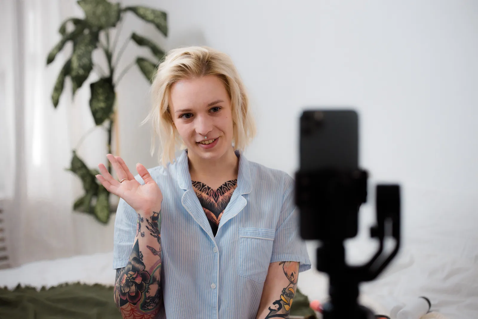 Tattooed woman with blonde hair smiling and recording video using a smartphone indoors