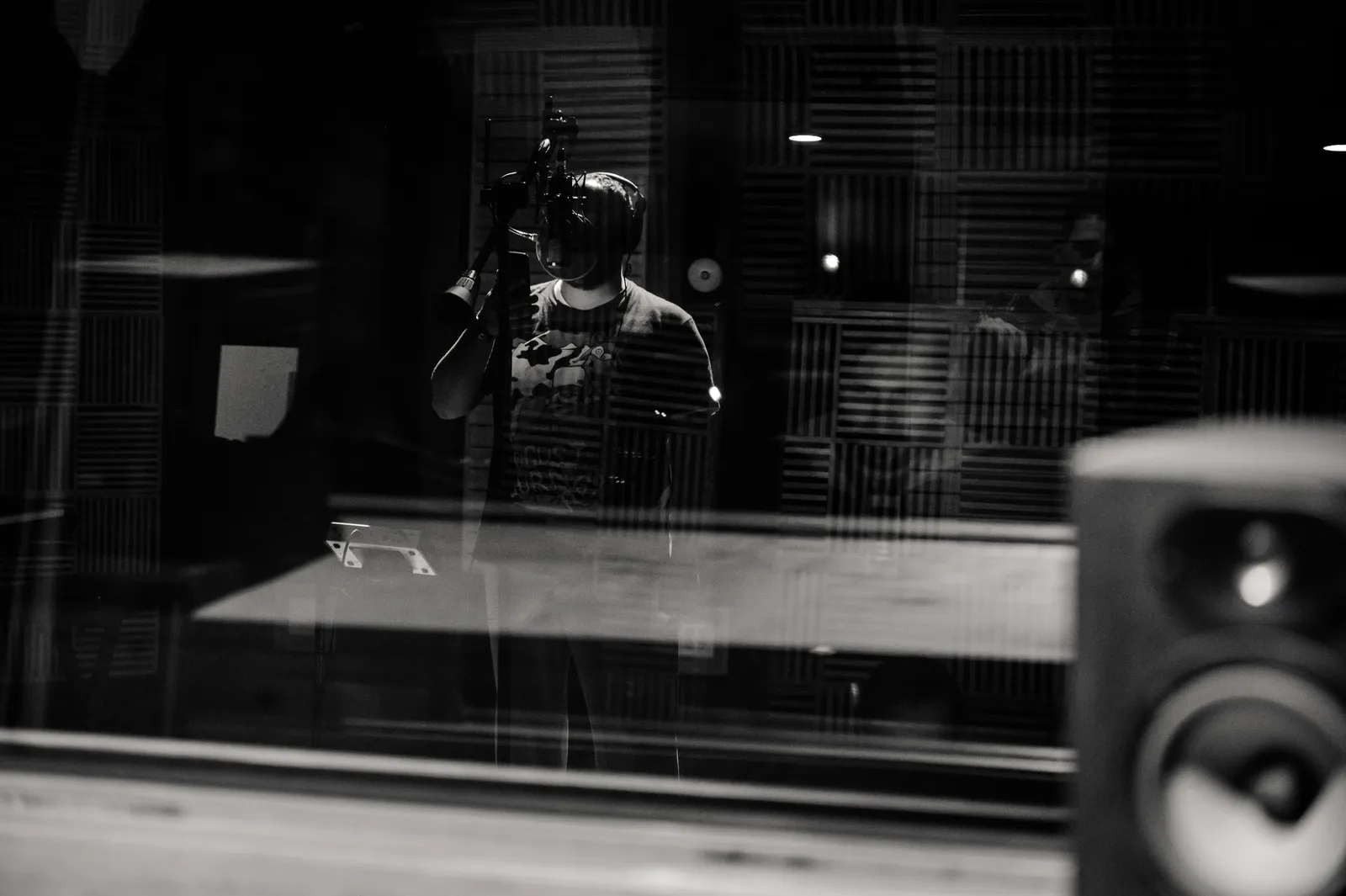 Through glass of black and white anonymous male musician in headphones singing with microphone while recording song in