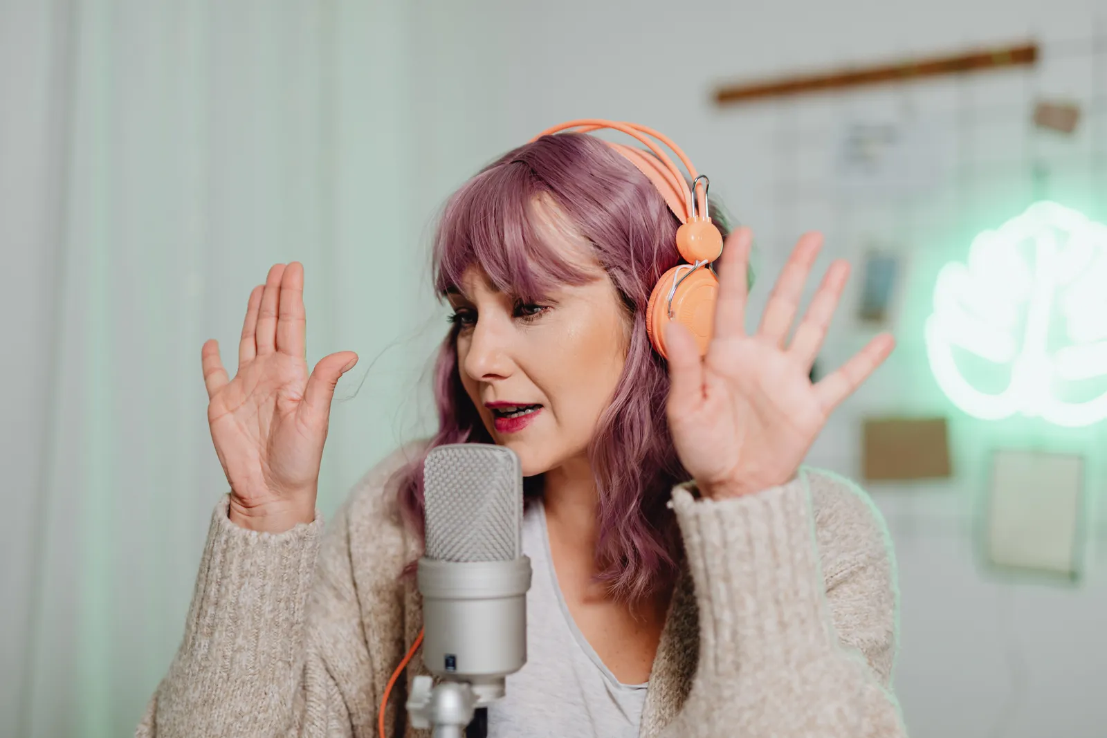 A woman podcasting in a studio setting with a microphone and headphones, gesturing expressively