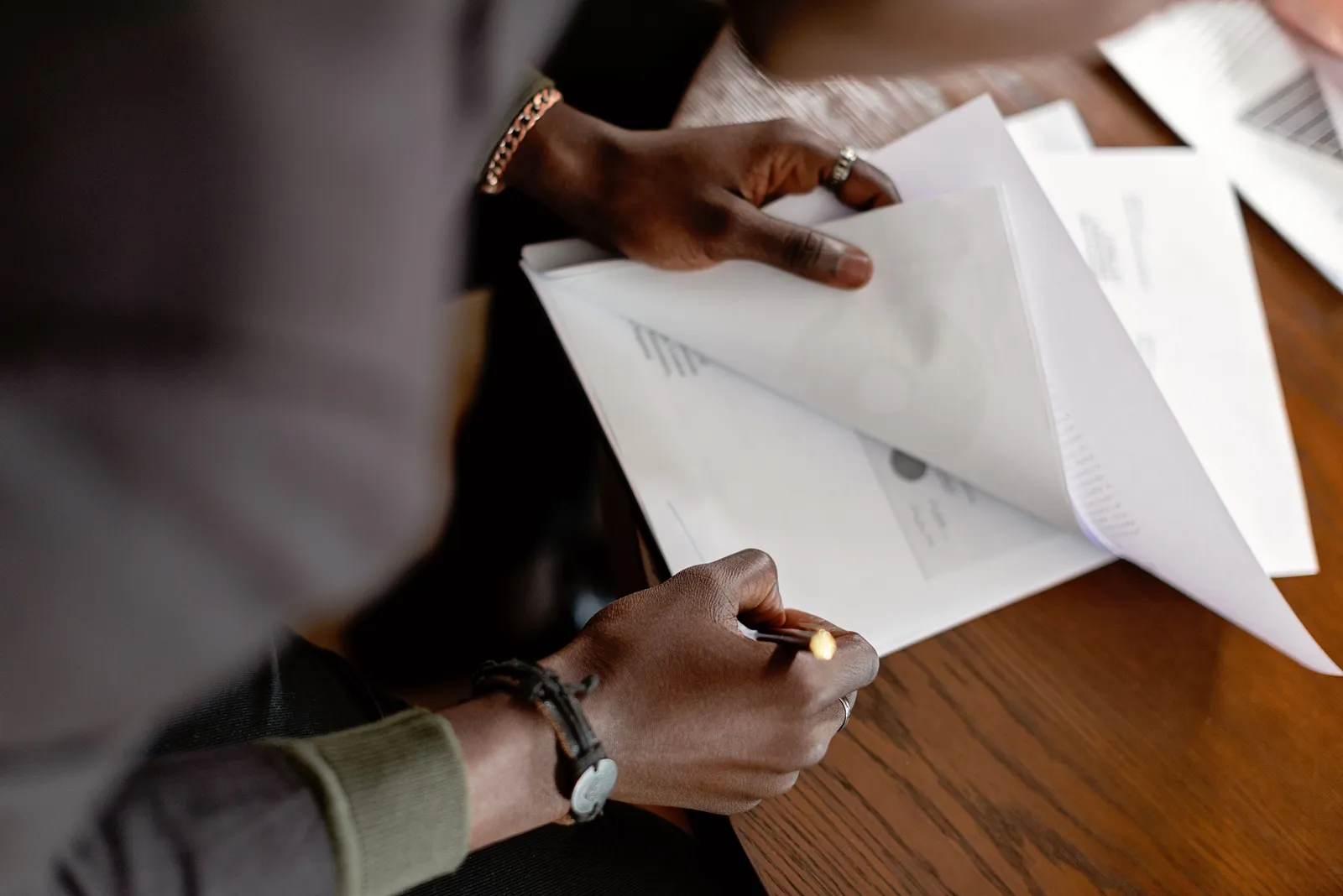 Adult revising papers with a pencil at a desk, focus on hands and documents
