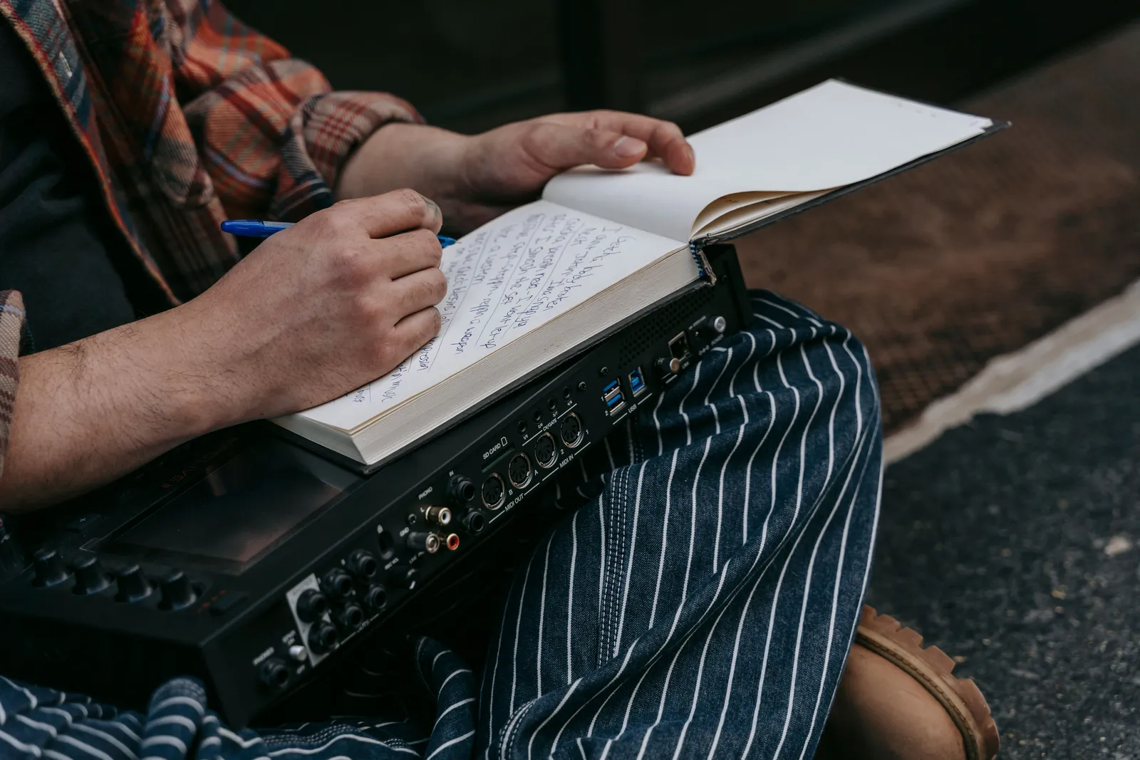 Close-up of a person sitting with a notebook, writing music notes, and holding audio equipment