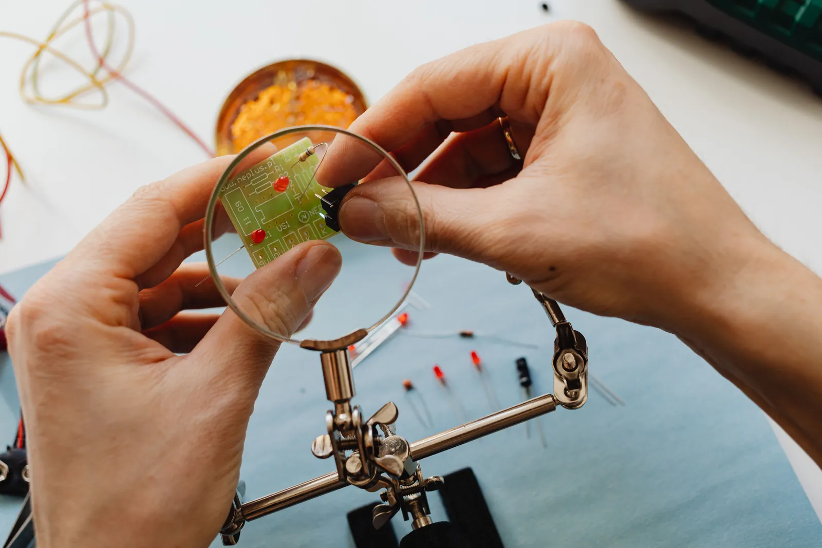 Close-up of hands using a magnifier to work on a circuit board with electronic components
