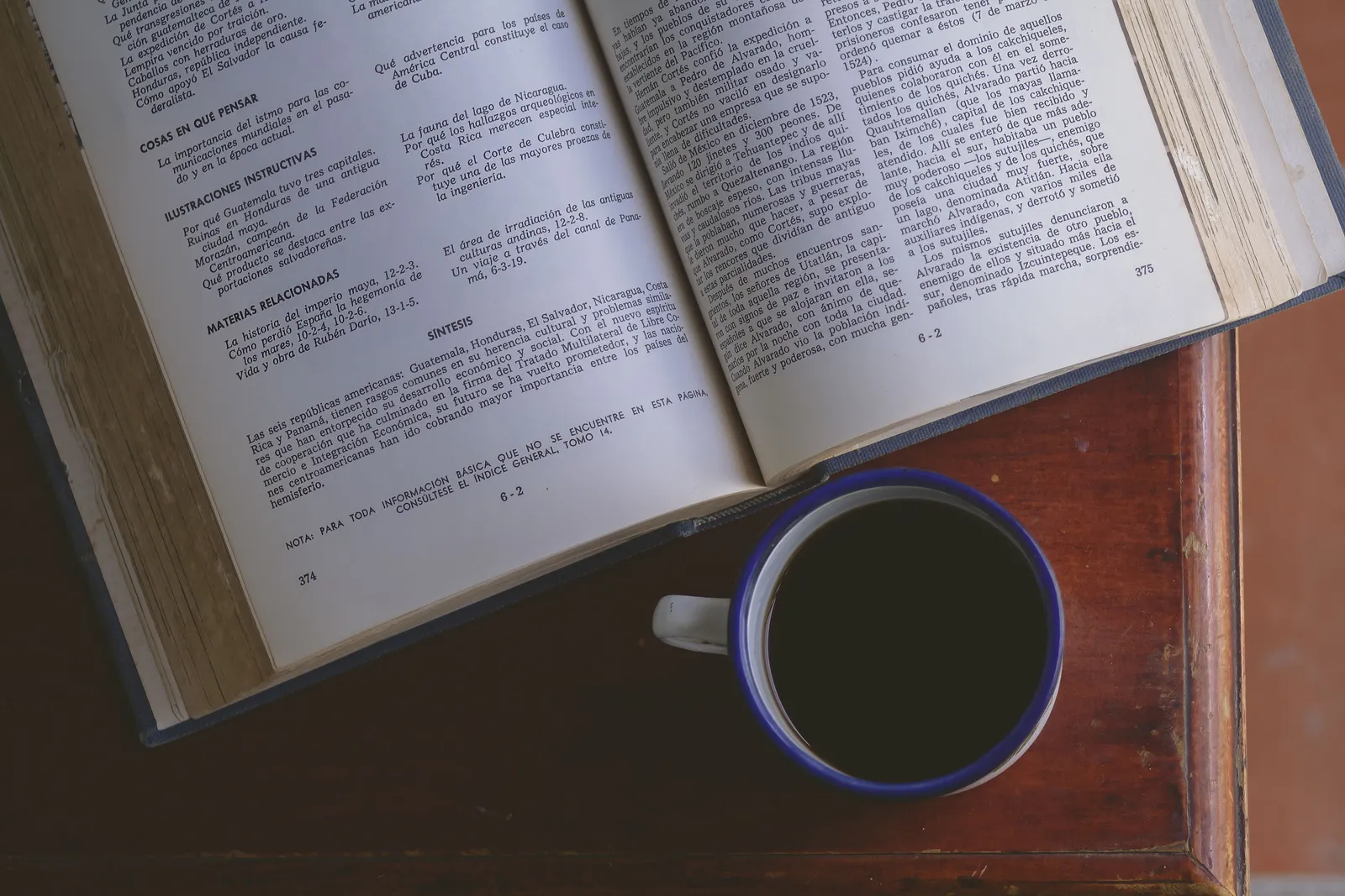 A top-down view of an open book with a cup of coffee on a wooden table in natural lighting