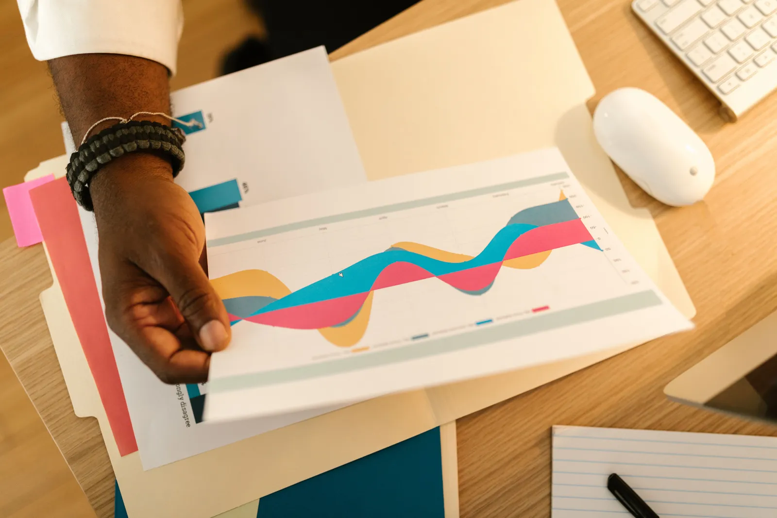 A person's hand holds a printed business graph paper on a desk with office supplies