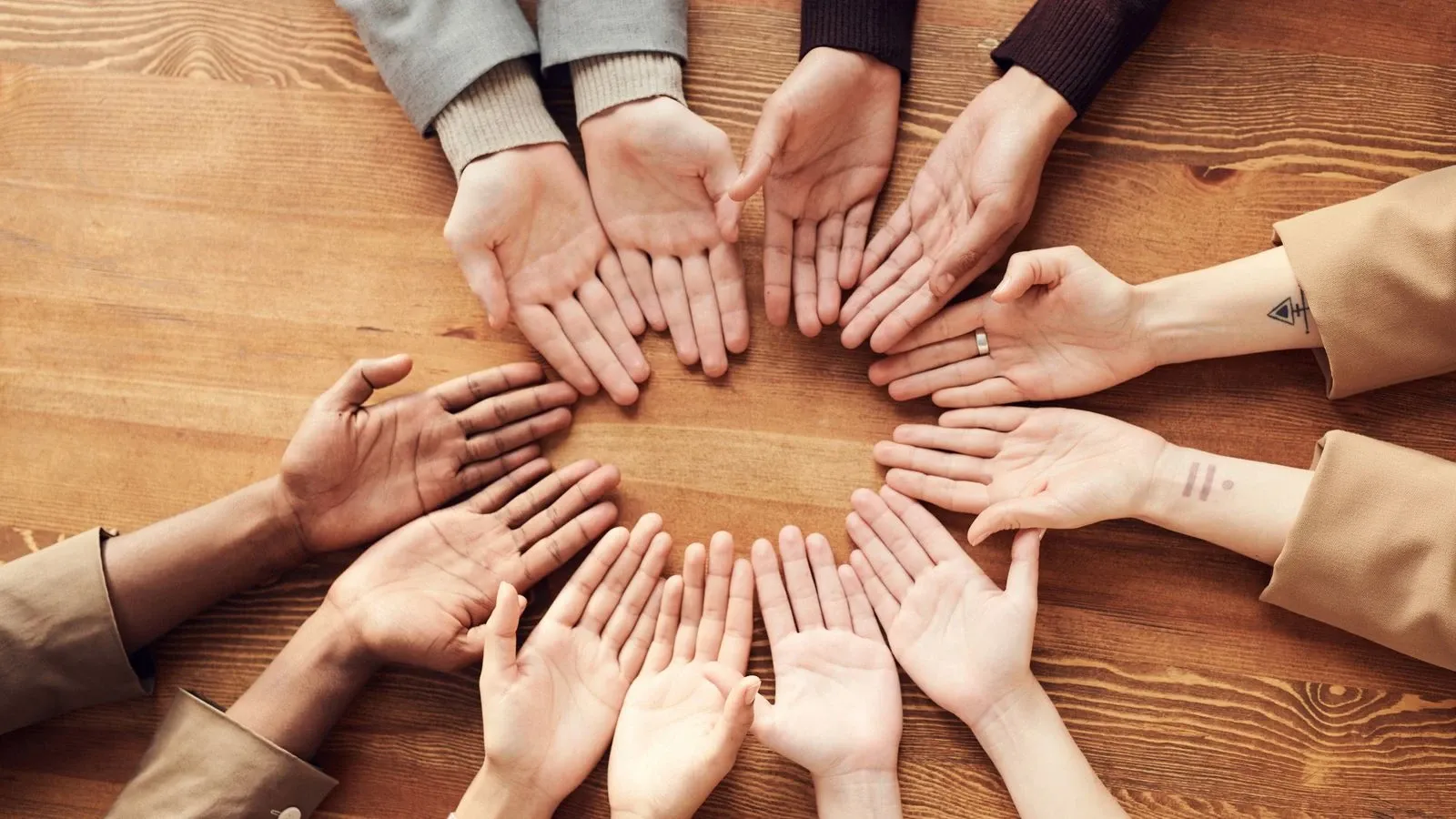 Open hands arranged in a circle on a wooden table