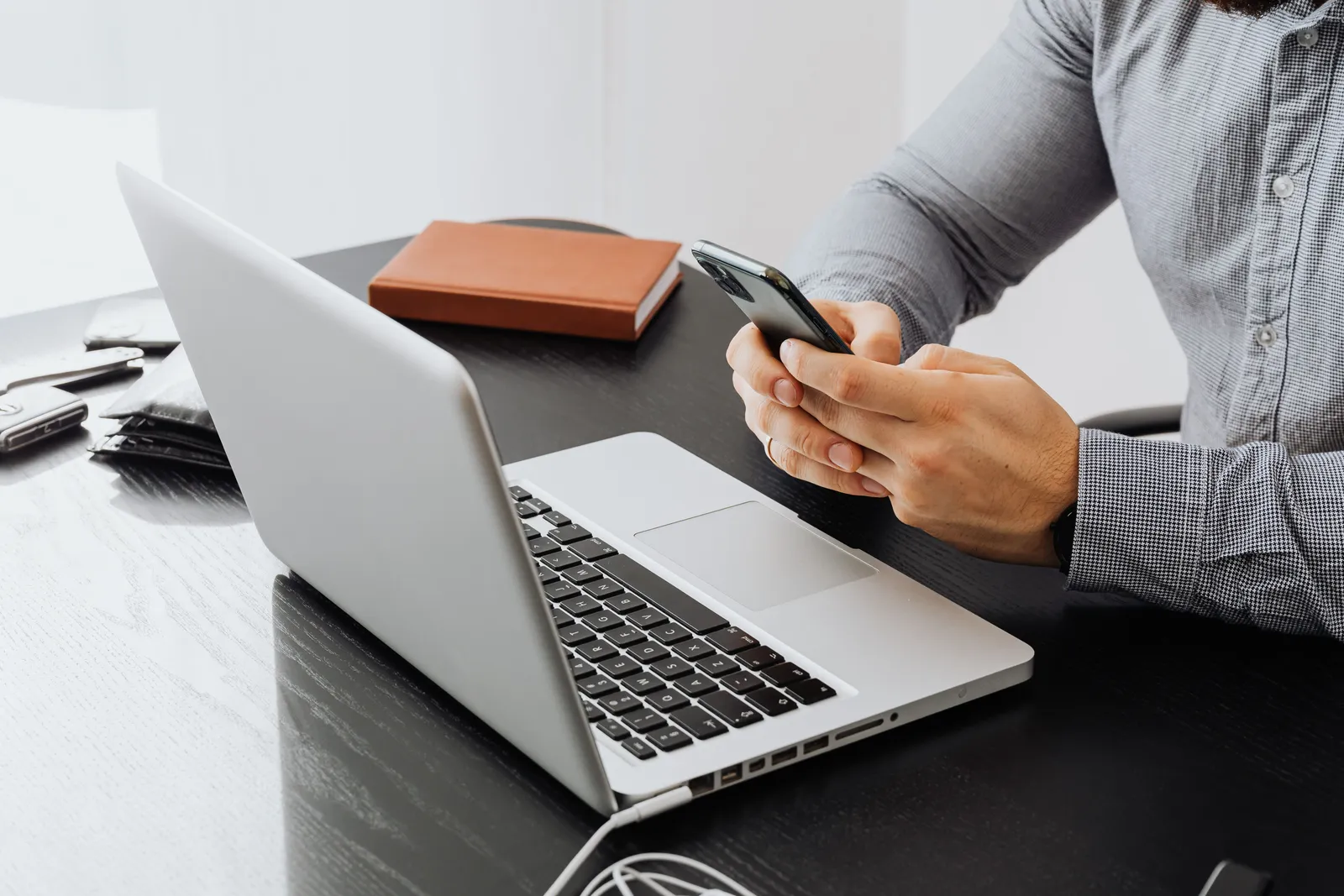 An adult using a smartphone at an office desk with a laptop for work