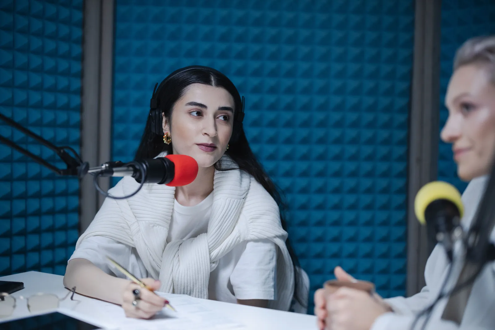 Two women engaged in a podcast recording with professional microphones, soundproof studio