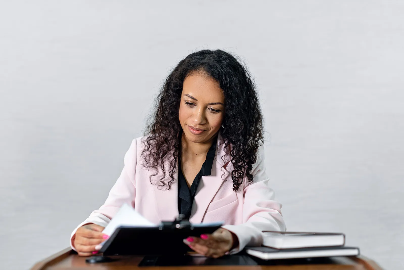 Confident woman with curly hair in a formal attire reviewing documents at a desk
