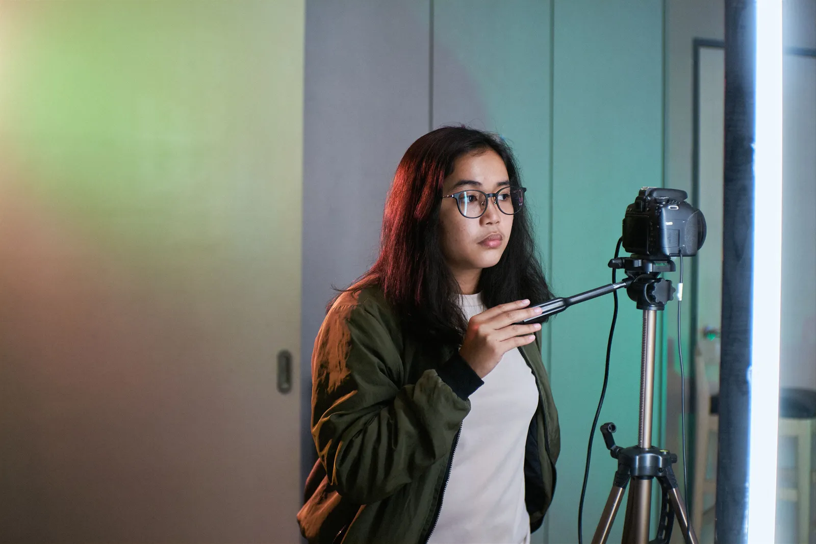 A young woman with glasses in a photography studio operating a camera on a tripod