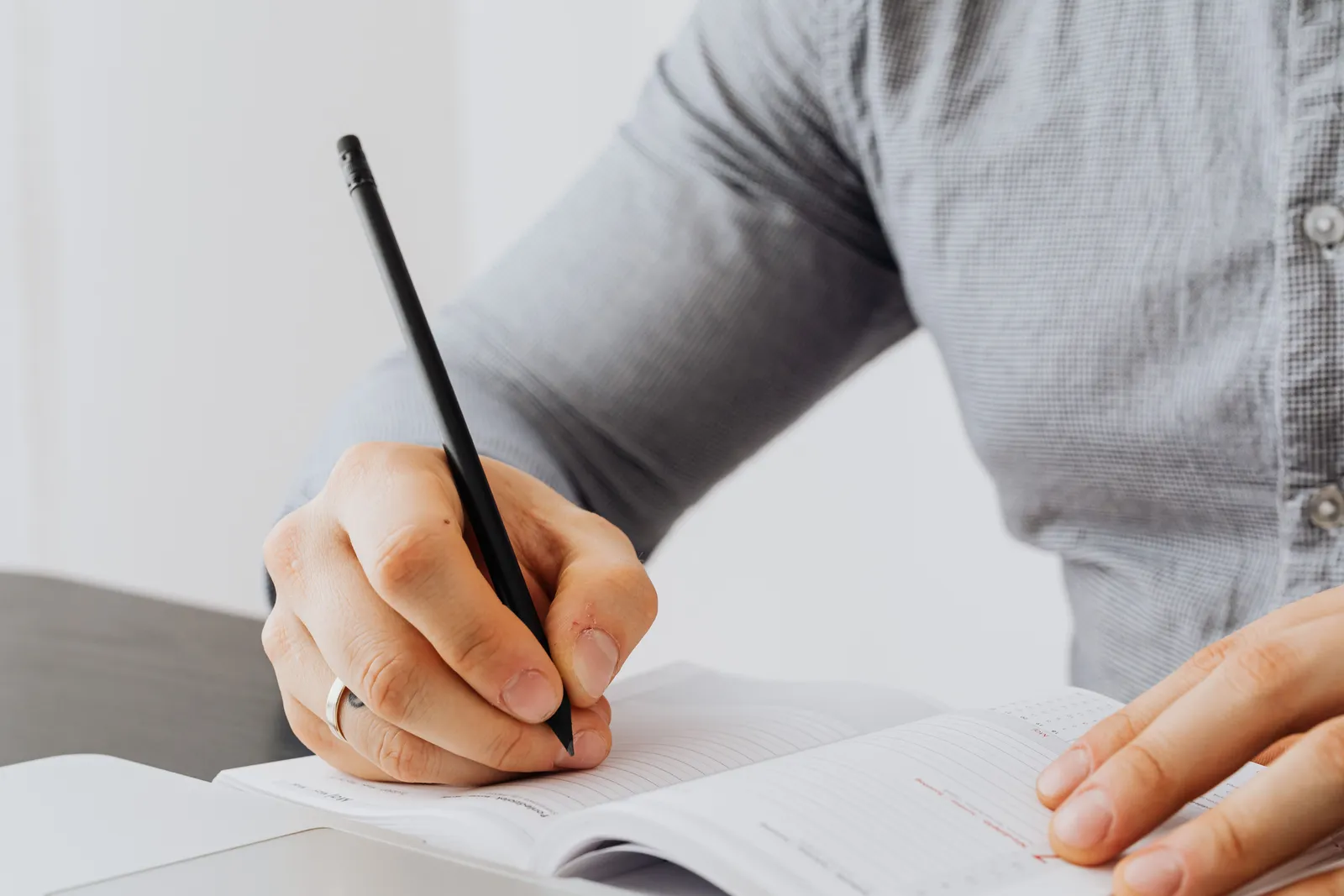 A detailed view of a person writing in a notebook with a pen, showing focus and concentration
