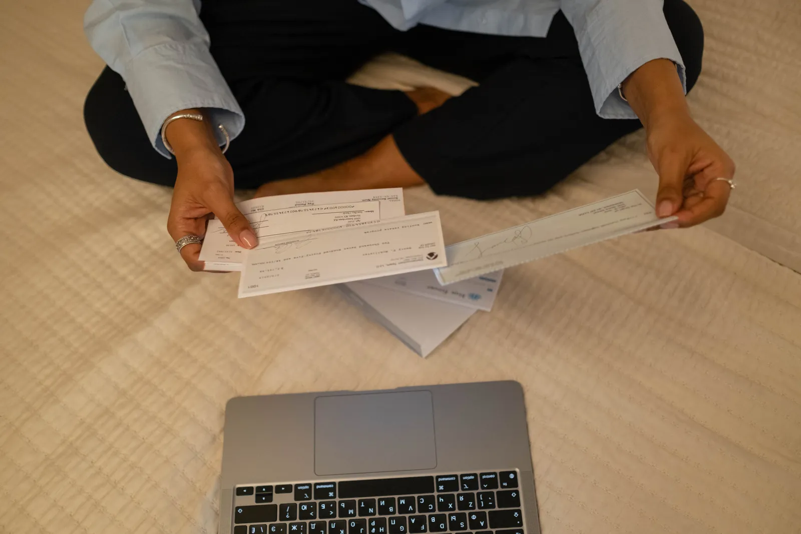 Close-up of hands holding cheques beside a laptop indoors for financial tasks