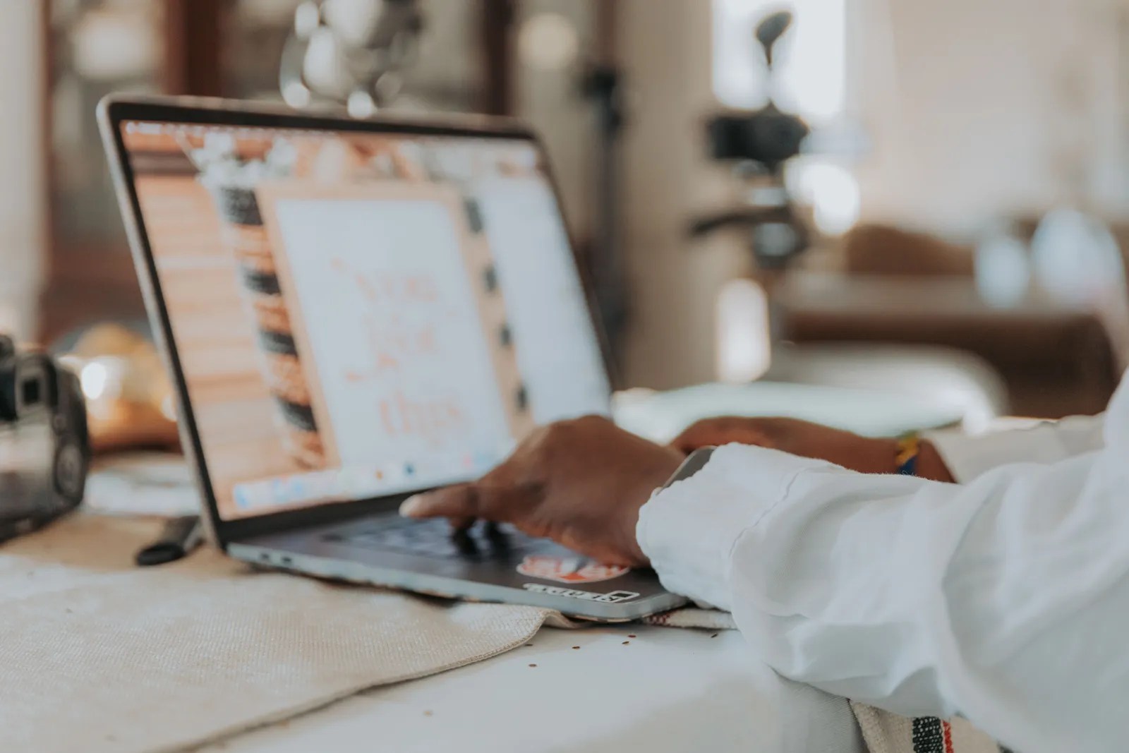 A person typing on a laptop with a blurred screen in a cozy home office setting