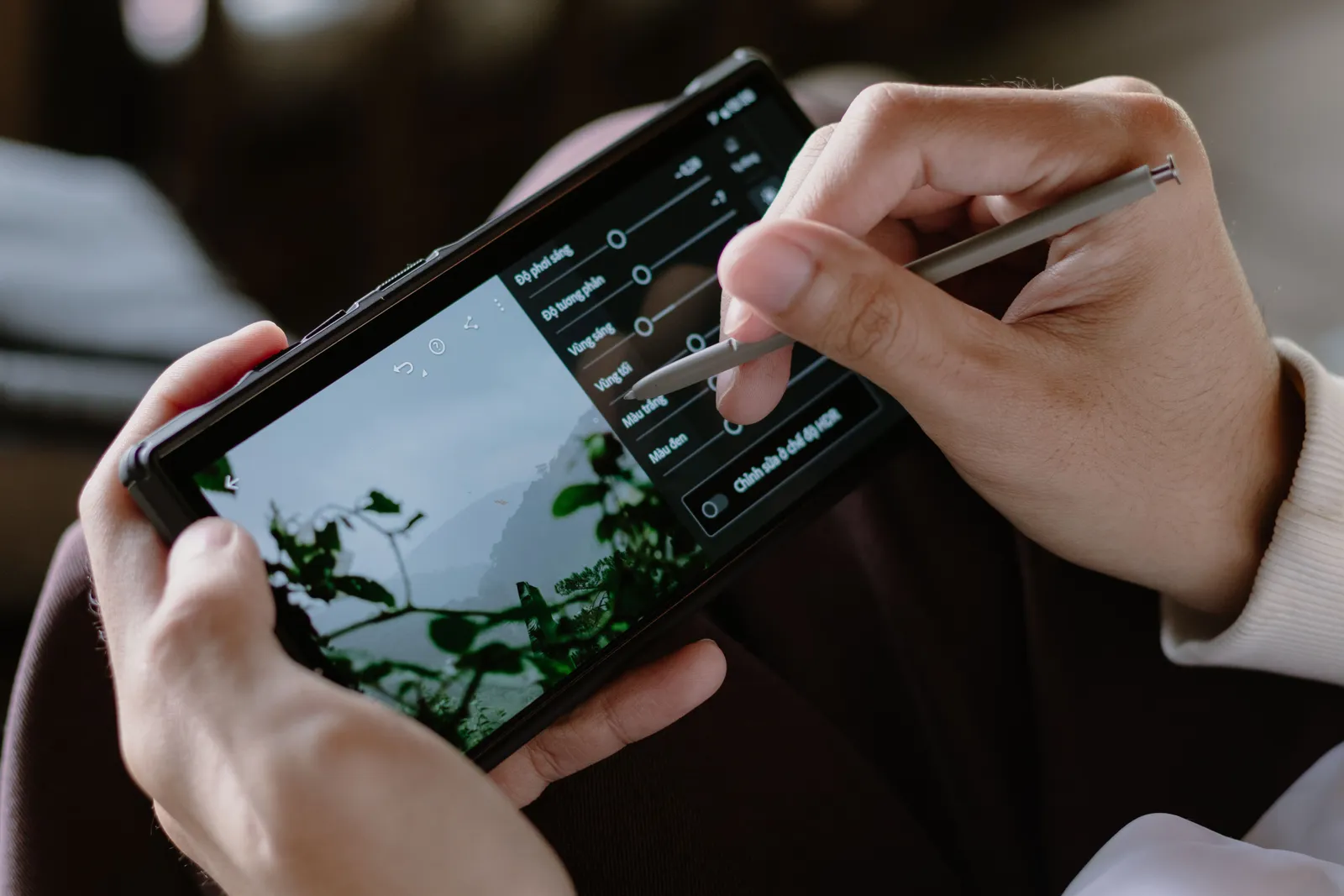 Close-up of a person editing photos on a smartphone with a stylus indoors