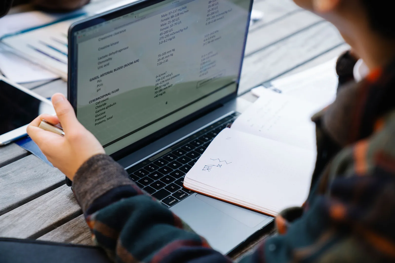 Close-up of hands using a laptop and taking notes at a wooden table